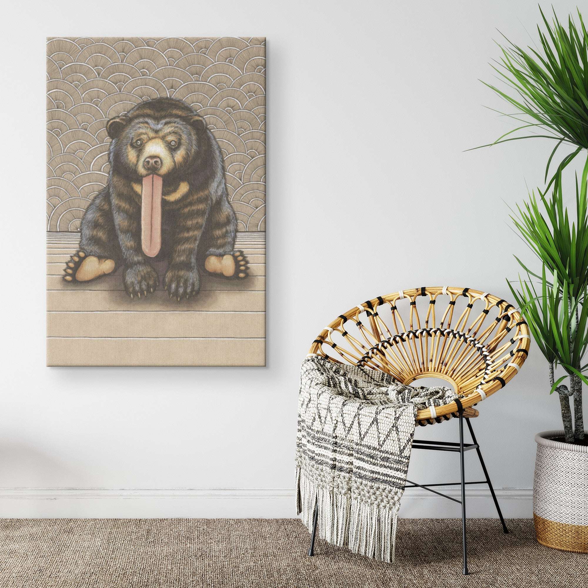 A whimsical Canvas Sun Bear Print depicting a bear with its tongue out, hanging on a white wall beside a stylish round chair with a patterned throw blanket.
