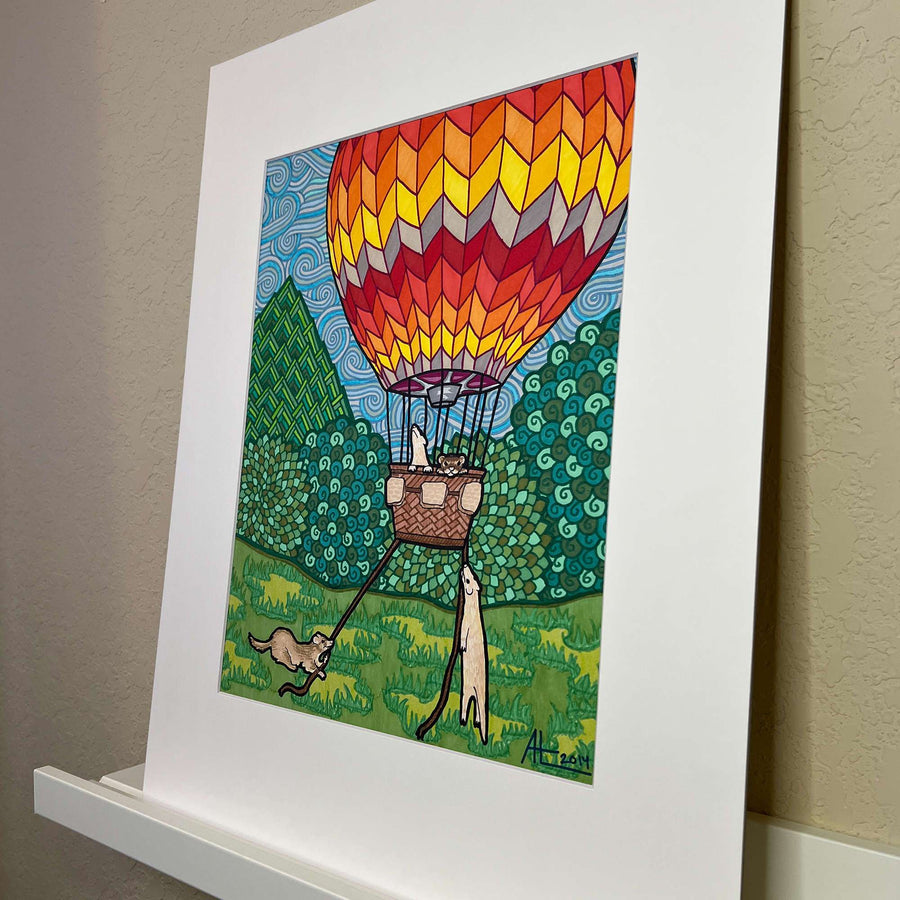 Angled close up view of marker artwork of a hot air balloon with ferrets on a white shelf against a neutral wall.