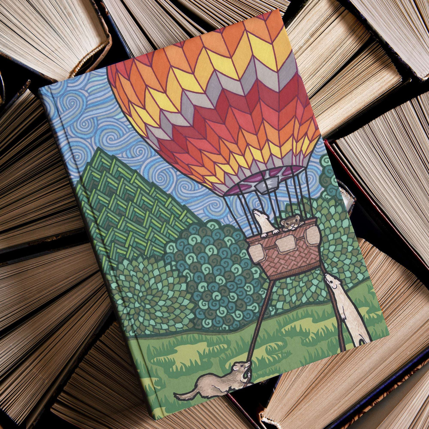 A Ferret Flight Journal with a hot air balloon and ferrets illustration on the cover, resting on a pile of old books.
