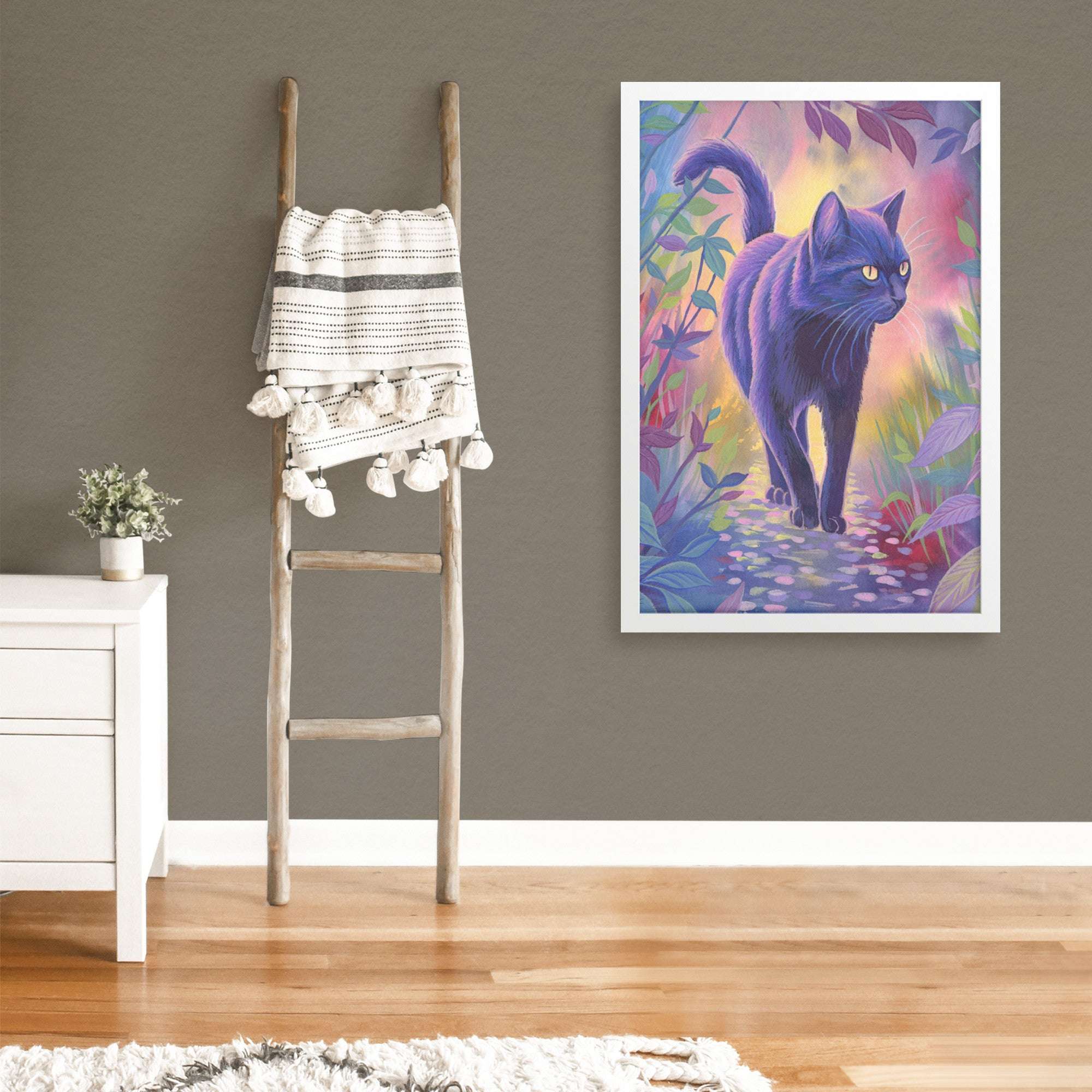 A colorful Framed Cat Art Print of a black cat in a vibrant forest is displayed on a gray wall beside a white side table.