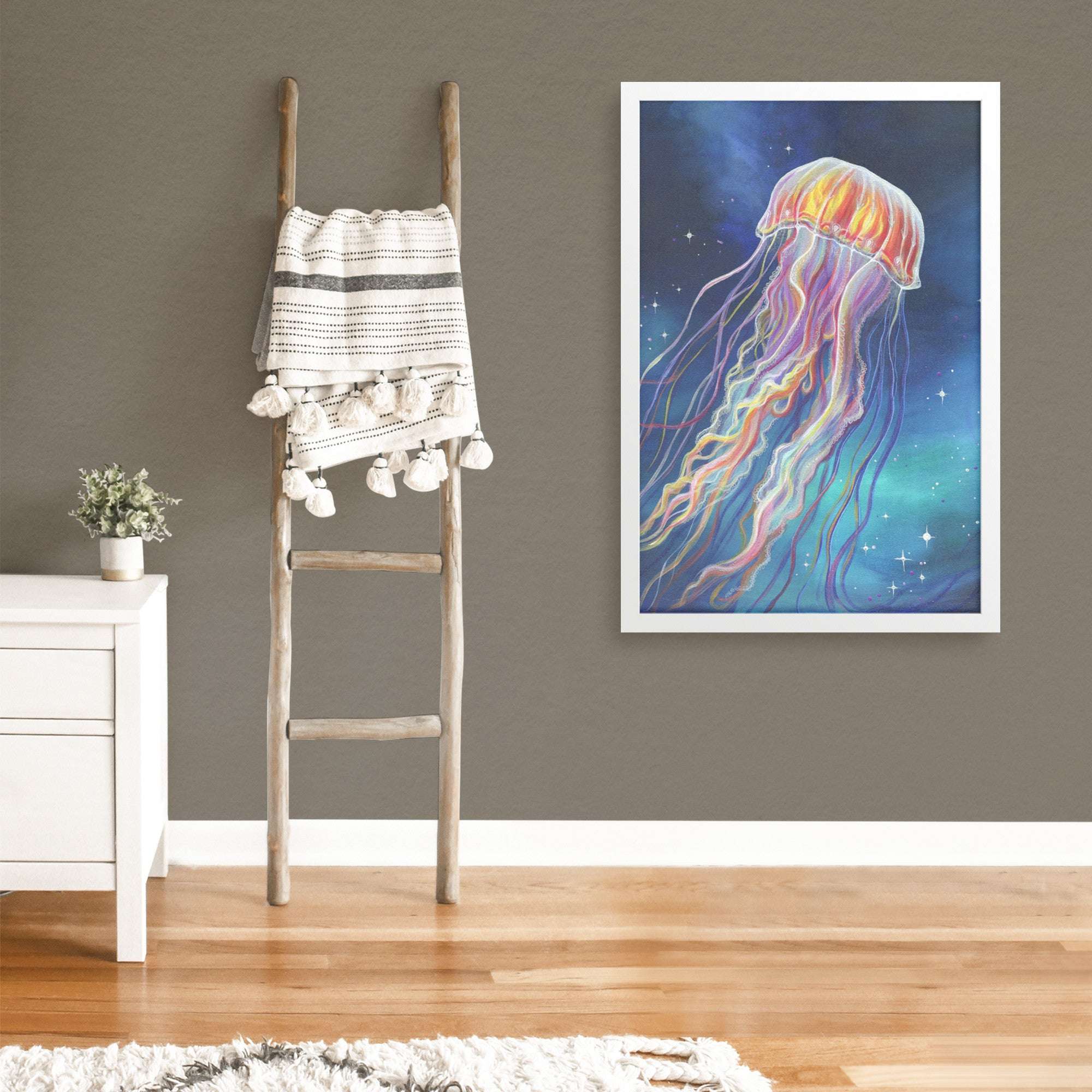 A large framed art print of a vibrant jellyfish on a grey wall, with a rustic ladder and throw nearby.