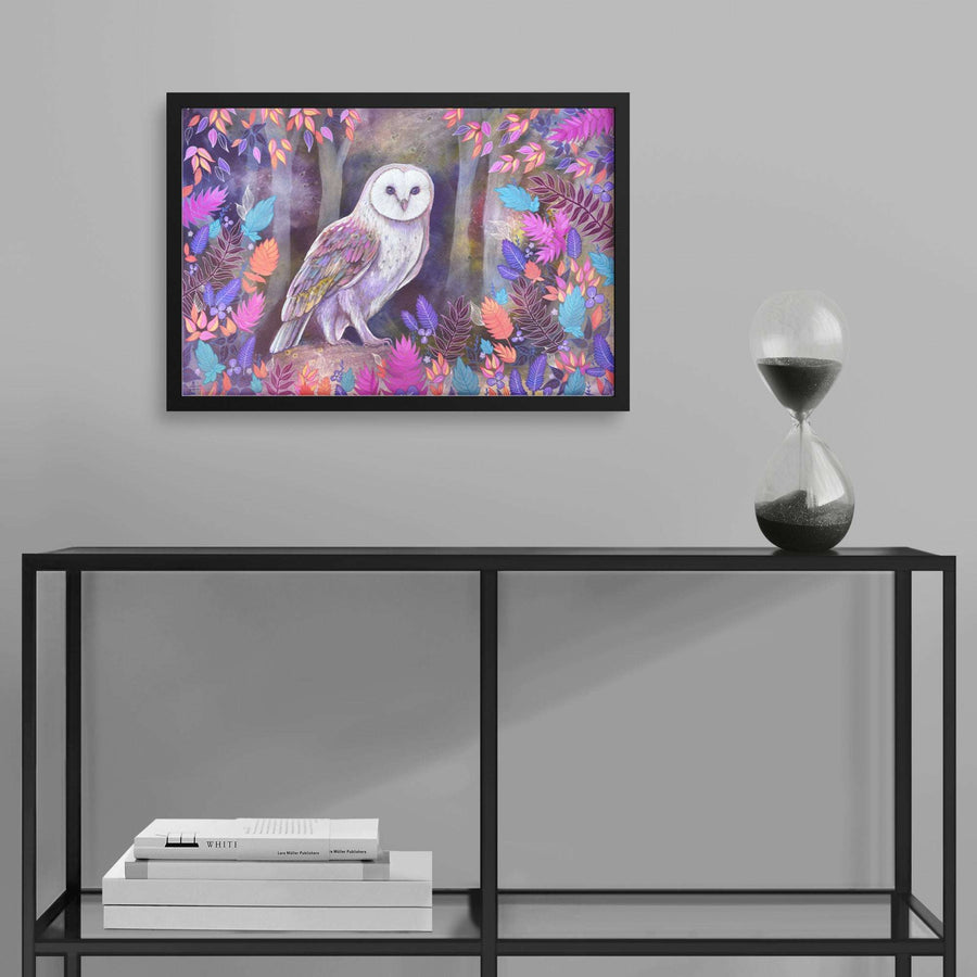 A Framed Owl Art Print of an barn owl perched in a floral setting displayed on a wall, with an hourglass on a shelf to the right and stacked books on the lower shelf.
