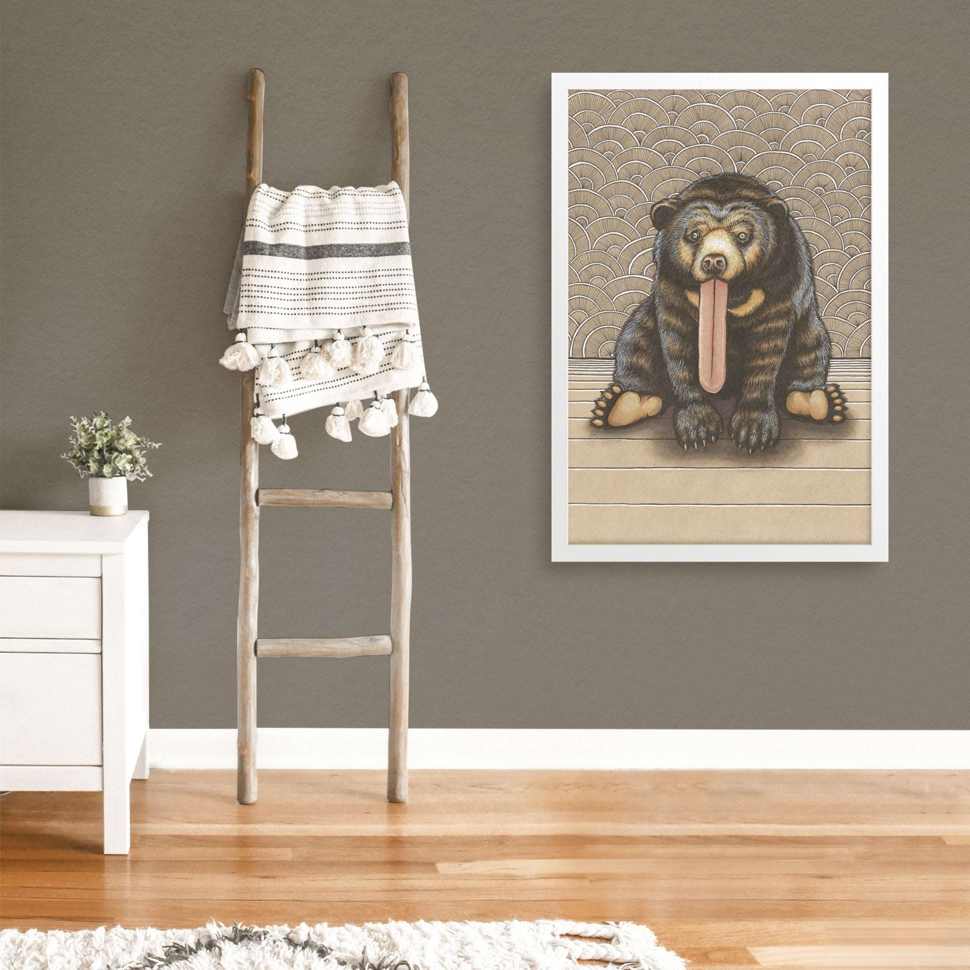 A Framed Sun Bear Art Print with its tongue out, hung on a gray wall.