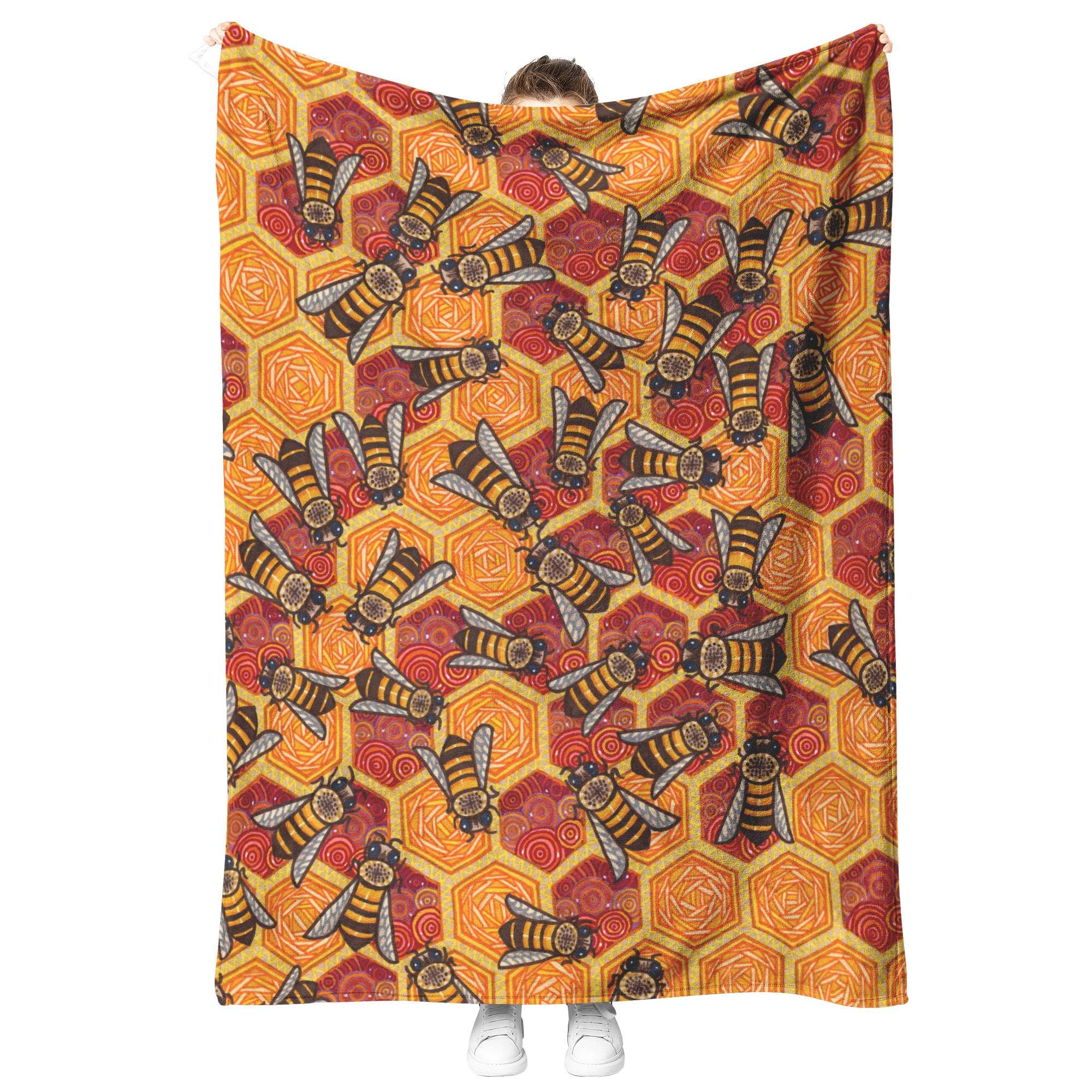 A person holding up a Honeycomb Harmony Blanket with a colorful geometric and bee pattern.
