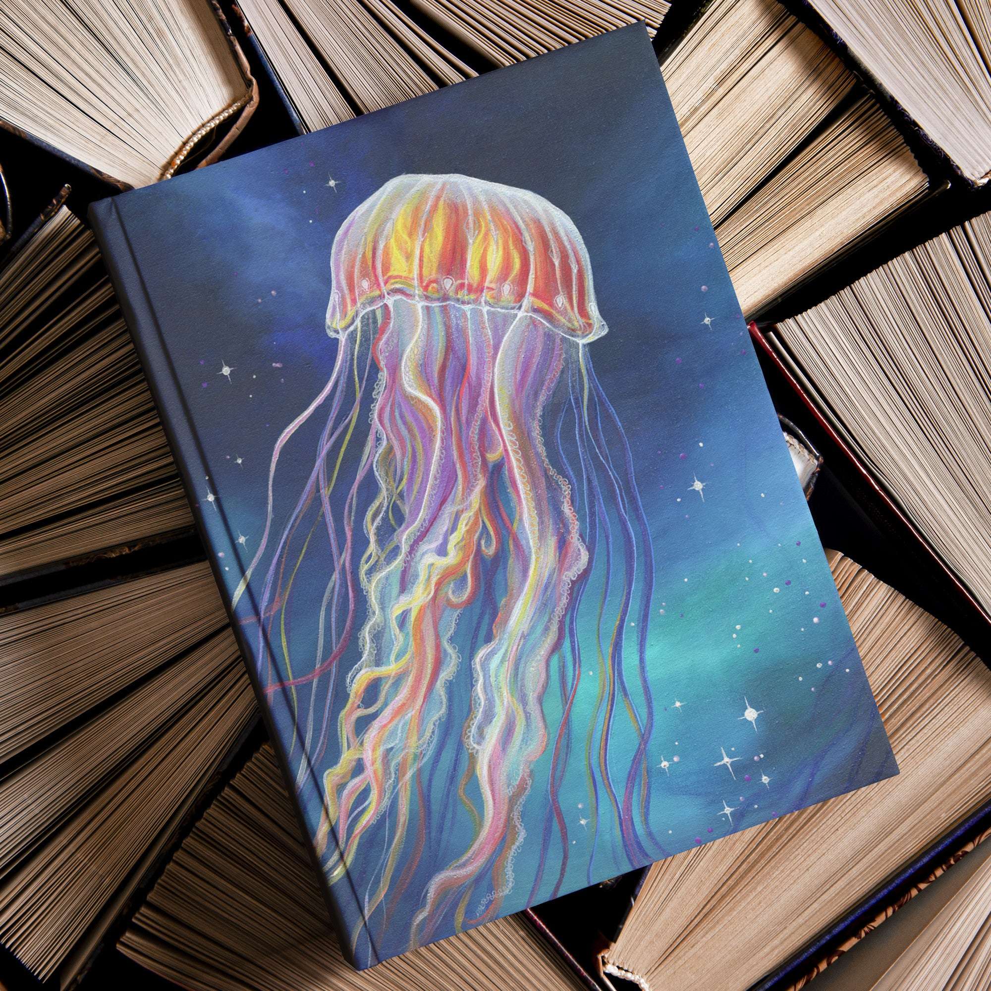 A Jellyfish Journal with a vibrant jellyfish illustration is placed on top of a stack of old books.