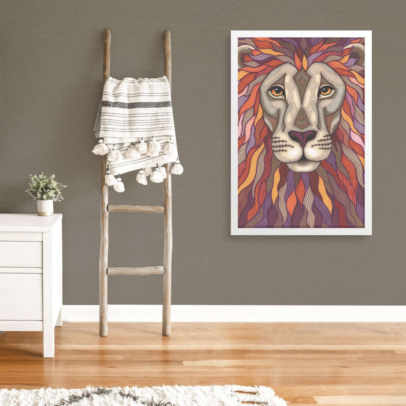 A modern room with gray walls featuring a Lion Pride Framed Print, a white cabinet, a wooden ladder with a blanket, and a small plant.