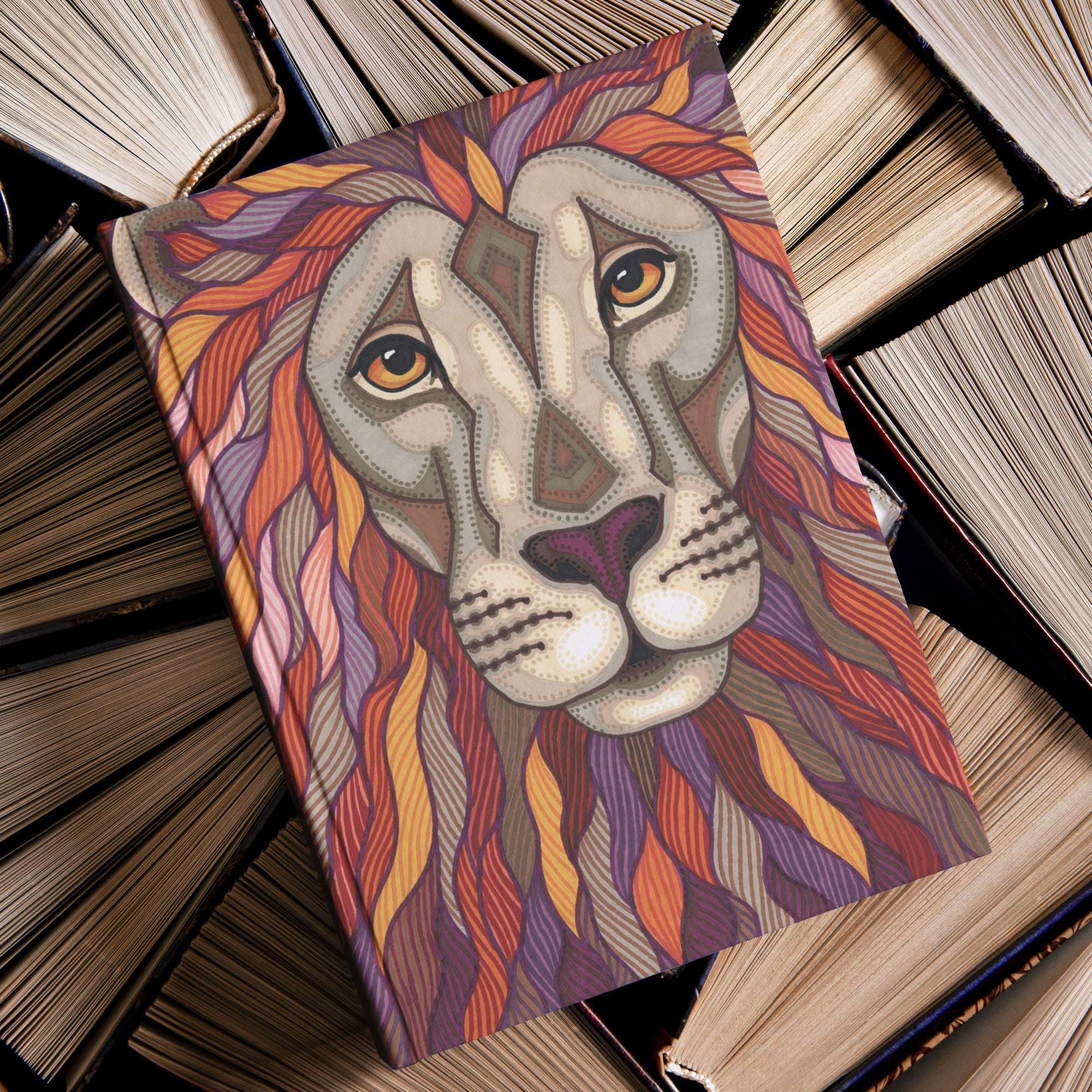 Illustrated Lion Pride Journal lies on top of a pile of old hardcover books.