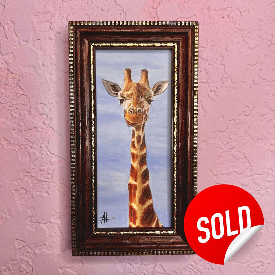Playful giraffe portrait in a vintage gold frame, with a red 'SOLD' sticker on a lavender wall.