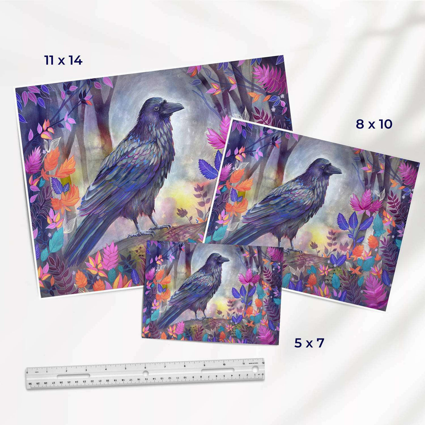 Various sizes of art prints depicting a raven among colorful leaves with a ruler for scale.