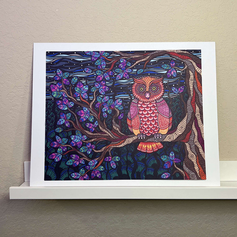 Colorful artwork of an Owl Tree perched on a branch amid vibrant, patterned foliage, displayed in a white frame on a shelf against a beige wall.