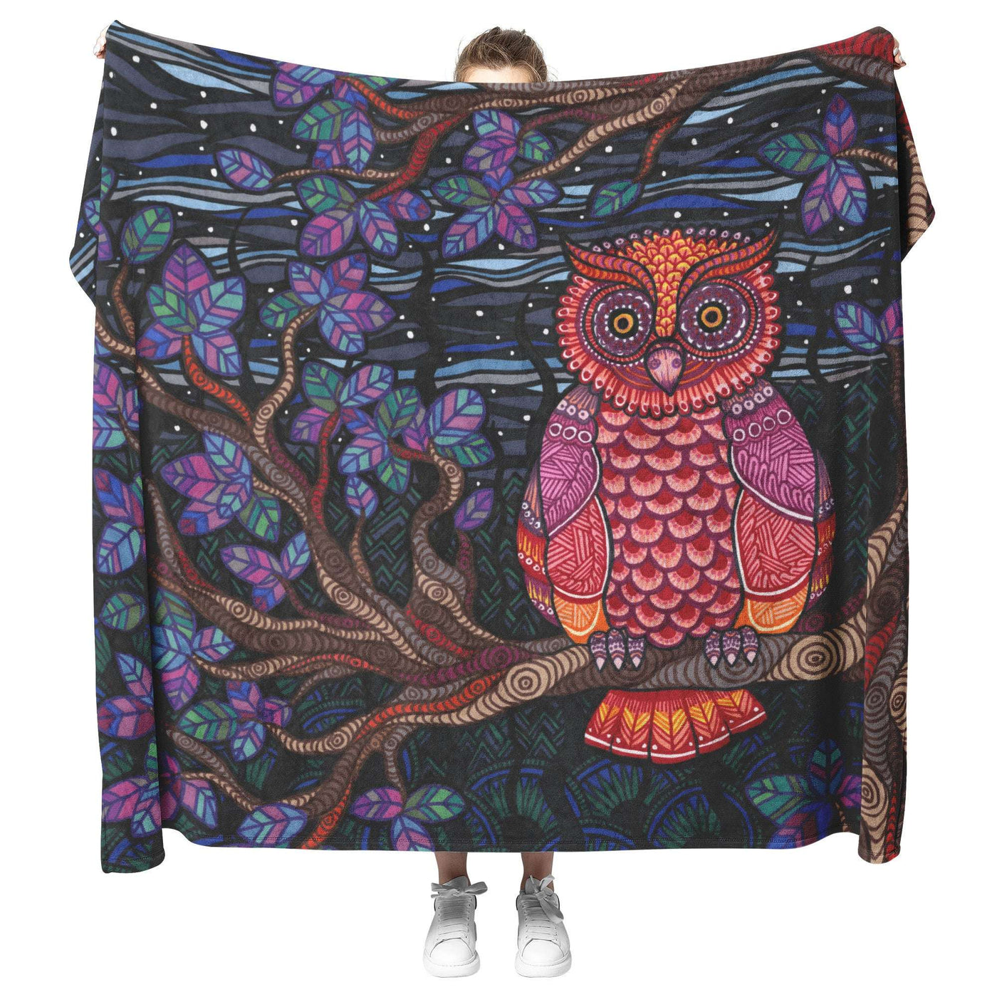 A person holding up a large, colorful Owl Tree Blanket featuring a detailed illustration of an owl on a tree branch with a starry night background.
