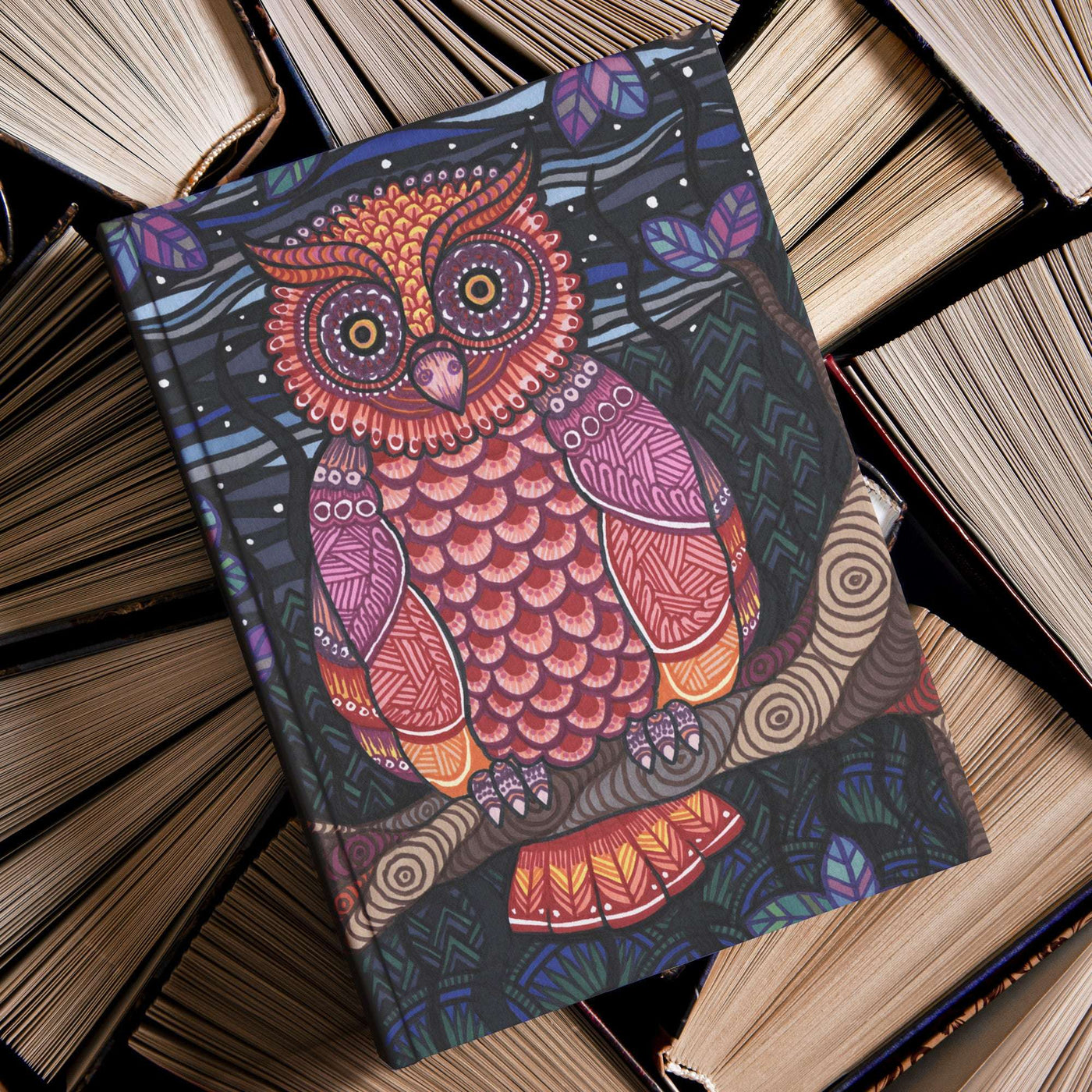 The colorful cover of an illustrated Owl Tree Journal, placed amidst a pile of old hardcover books.