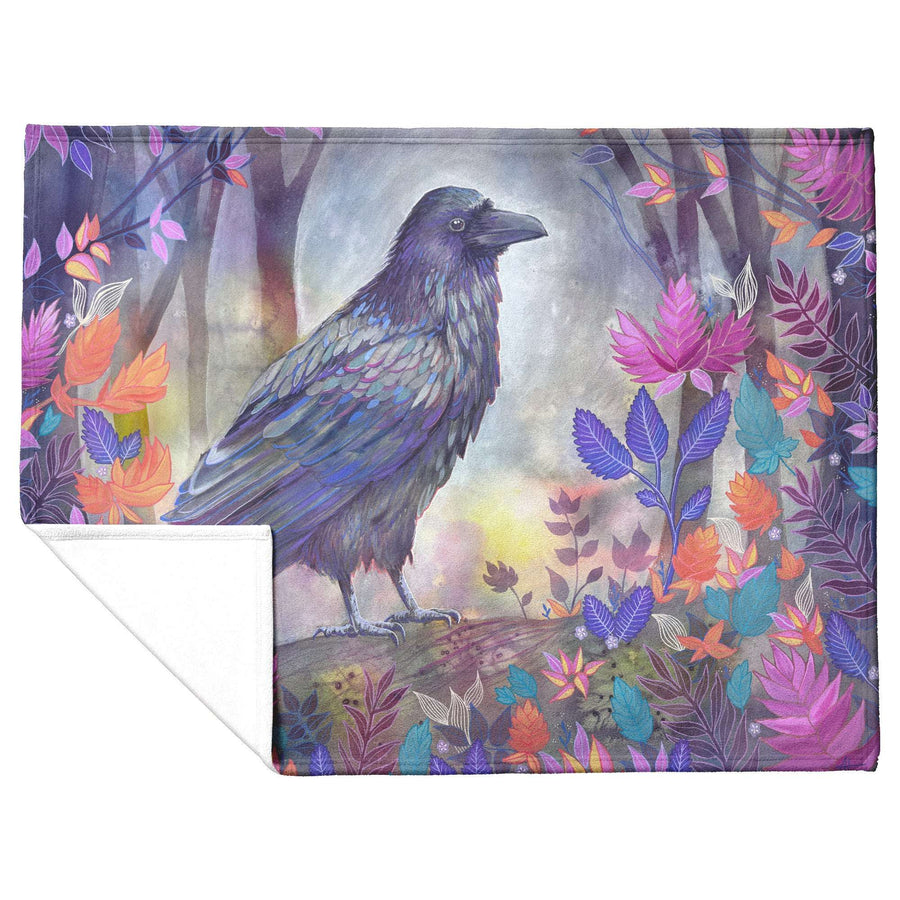 A vibrant Raven Blanket featuring an illustration of a raven perched on a branch in a colorful, mystical forest with various flowers and fog.
