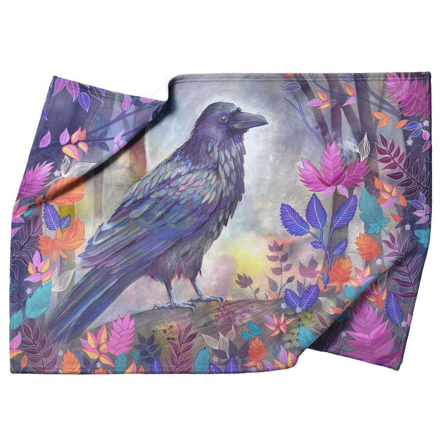 A Fleece Raven Blanket featuring an artistic illustration of a black raven among colorful leaves, set against a misty, ethereal background.