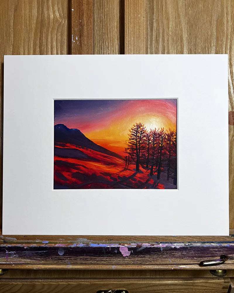Red Snow Sunset - Original Oil Painting of a sunset with silhouetted trees and a mountain, framed and resting on an easel surrounded by paint smudges.
