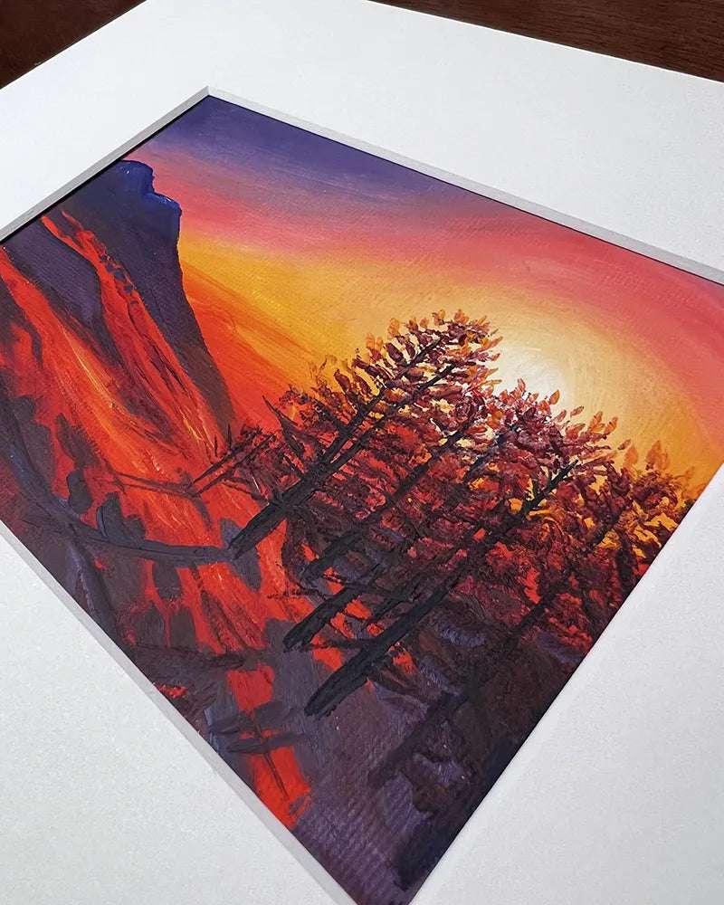 A vibrant painting of a Red Snow Sunset over a rocky landscape and silhouetted pine trees, displayed on a white matte board.