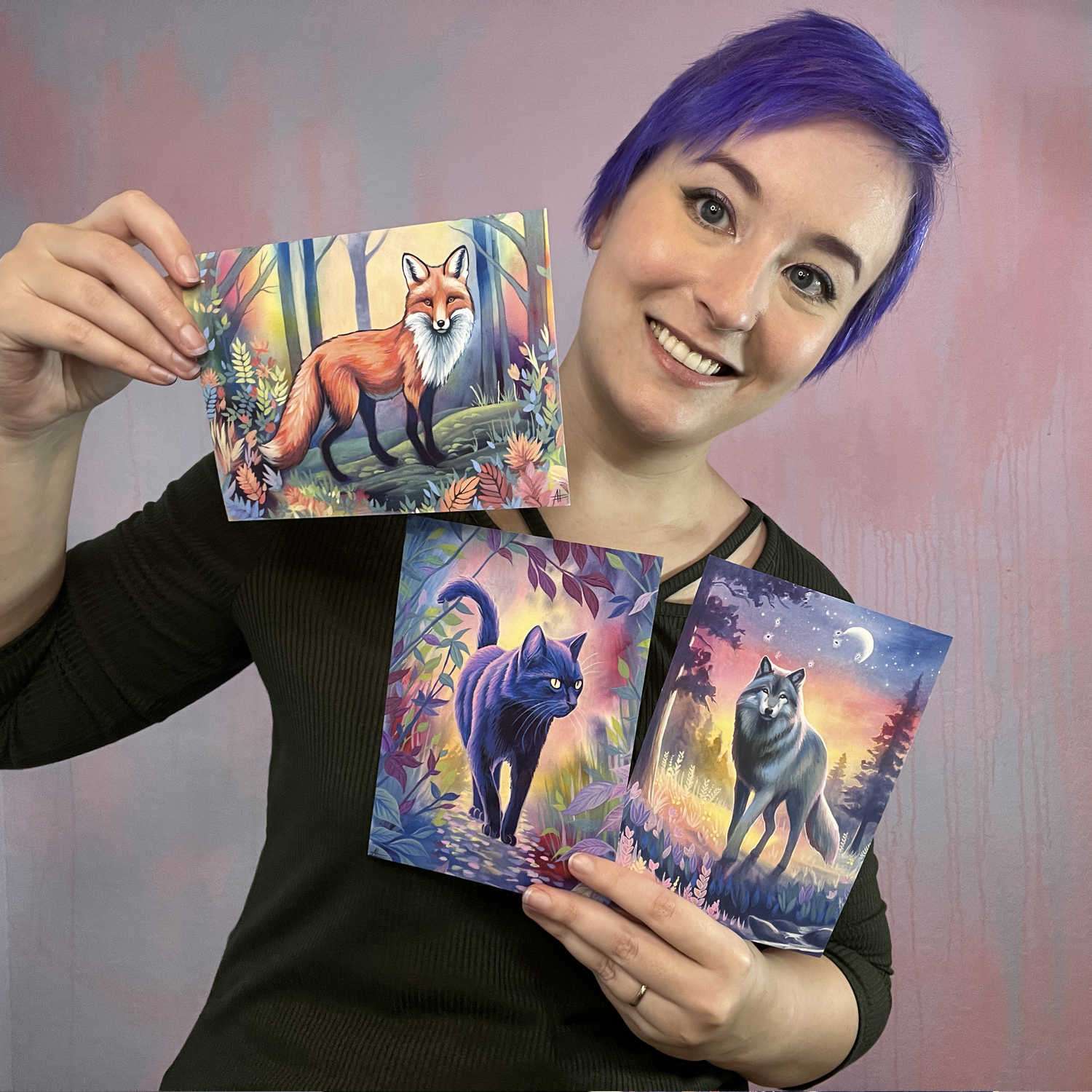 A woman with purple hair smiling and holding three small art prints of a wolf, cat, and fox from the Twilight Watch - Fine Art Print Bundle