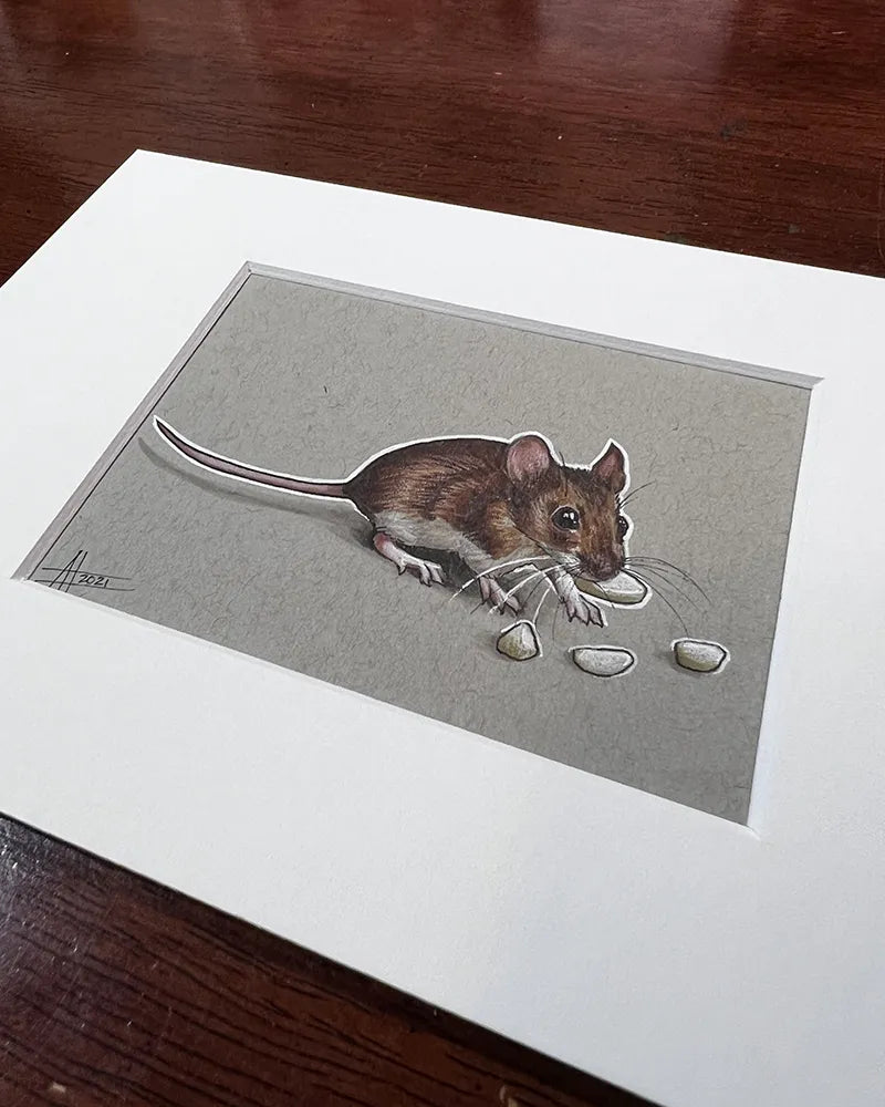 A realistic drawing of a tiny brown mouse on a beige paper framed with a white border, placed on a wooden table.