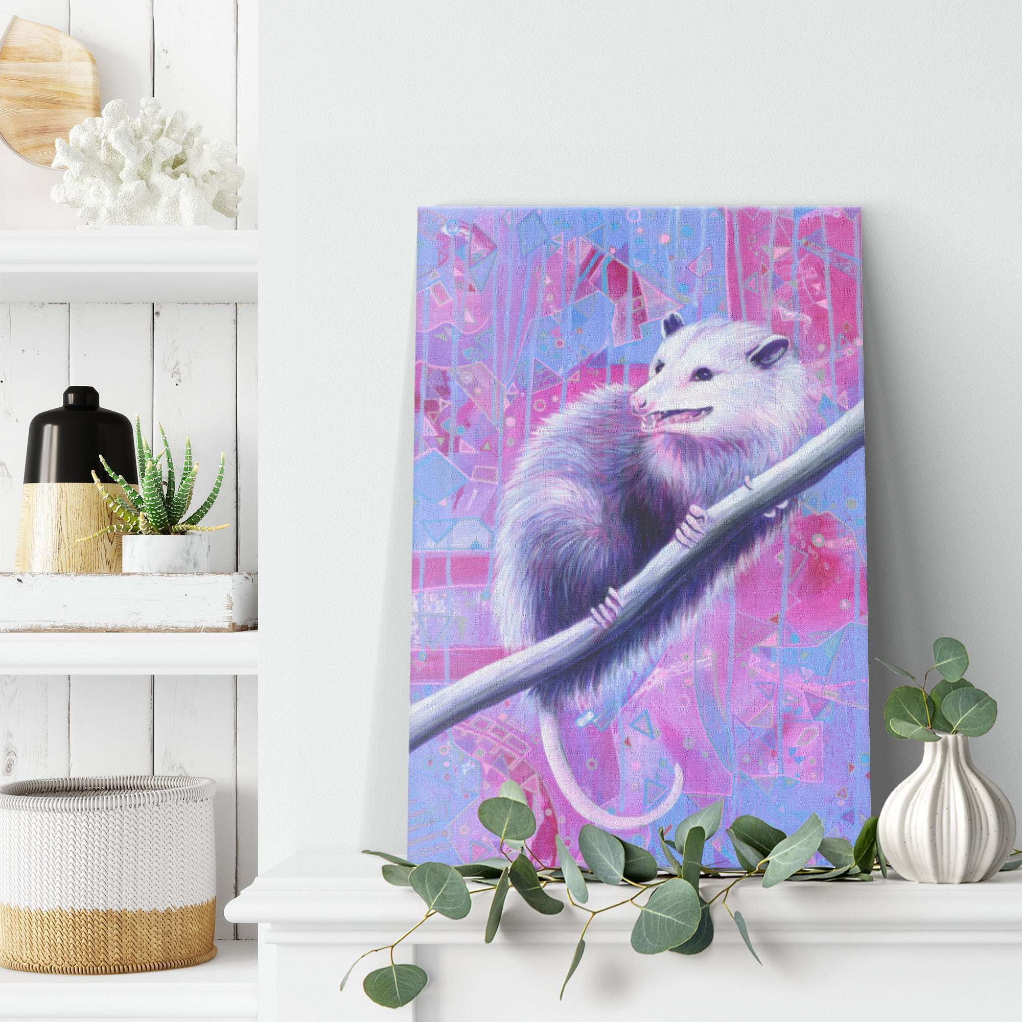 Canvas Art Print of a smiling opossum on a pink and blue abstract background, displayed on a white wall above a shelf with decorative items.