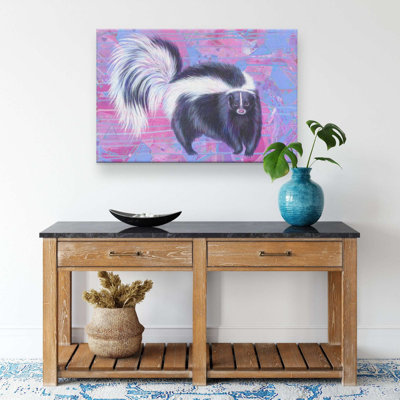 A Canvas Skunk Art Print of a skunk on a pink and blue background hangs above a wooden table.