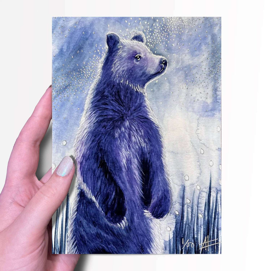 Hand holding a small art print of a blue bear with a starry background.