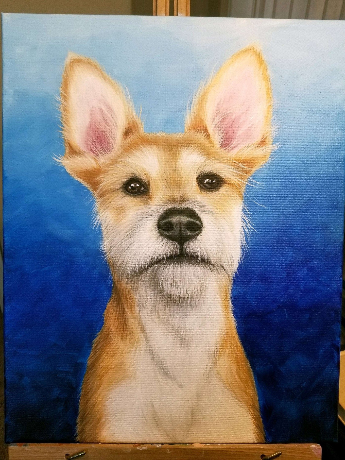 Acrylic pet portrait painting of a brown and white dog against a blue backdrop, presented on an easel.