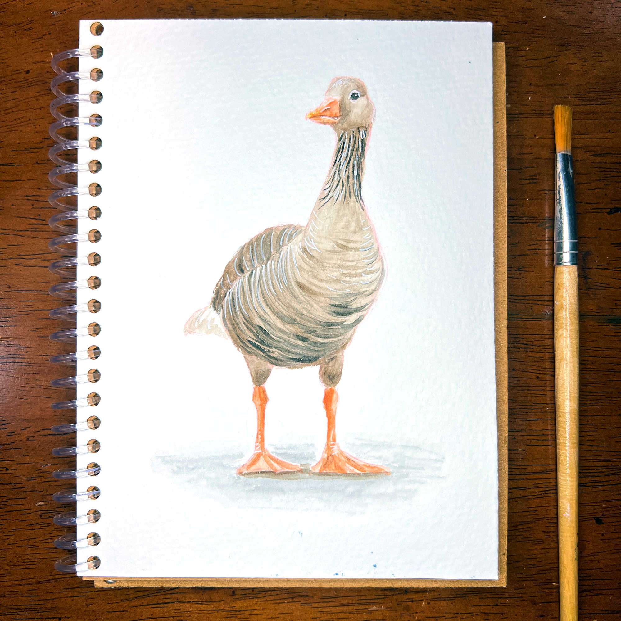 Watercolor sketch of a goose on a notepad next to a paintbrush.