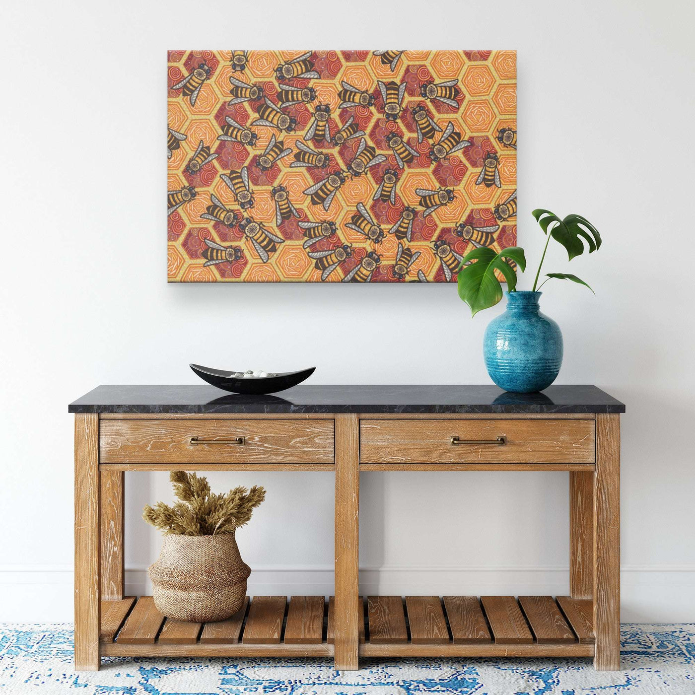 A wooden console table with two drawers, decorated with a patterned rug underneath, a blue vase with a plant, and a dry floral arrangement. The Honeycomb Harmony Canvas Print hangs above.