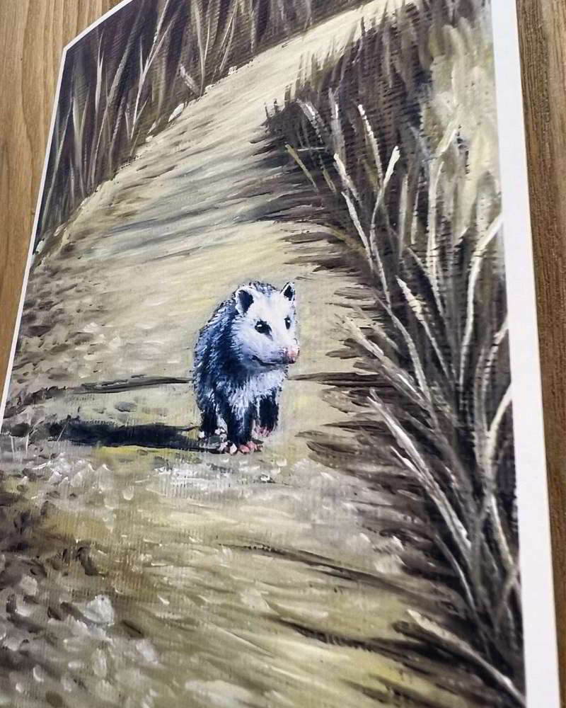 Angled view of a small opossum artwork on a wooden surface.
