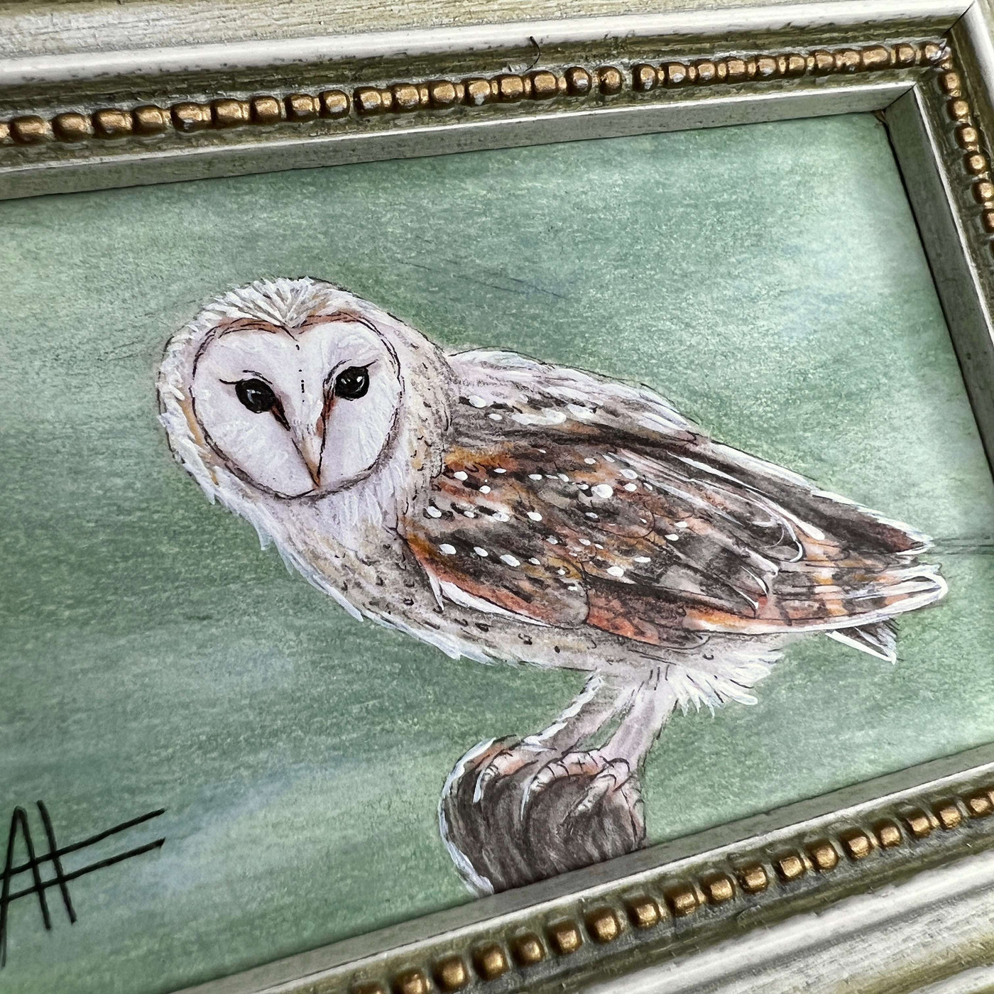 Zoom on owl painting in an ornate frame, highlighting its eyes and feathers.