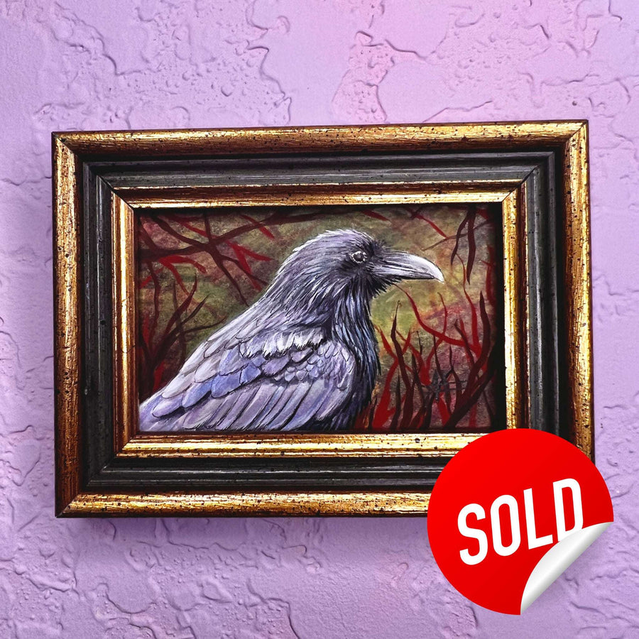 A miniature raven painting in a weathered frame on a purple wall, with a 'SOLD' sticker.