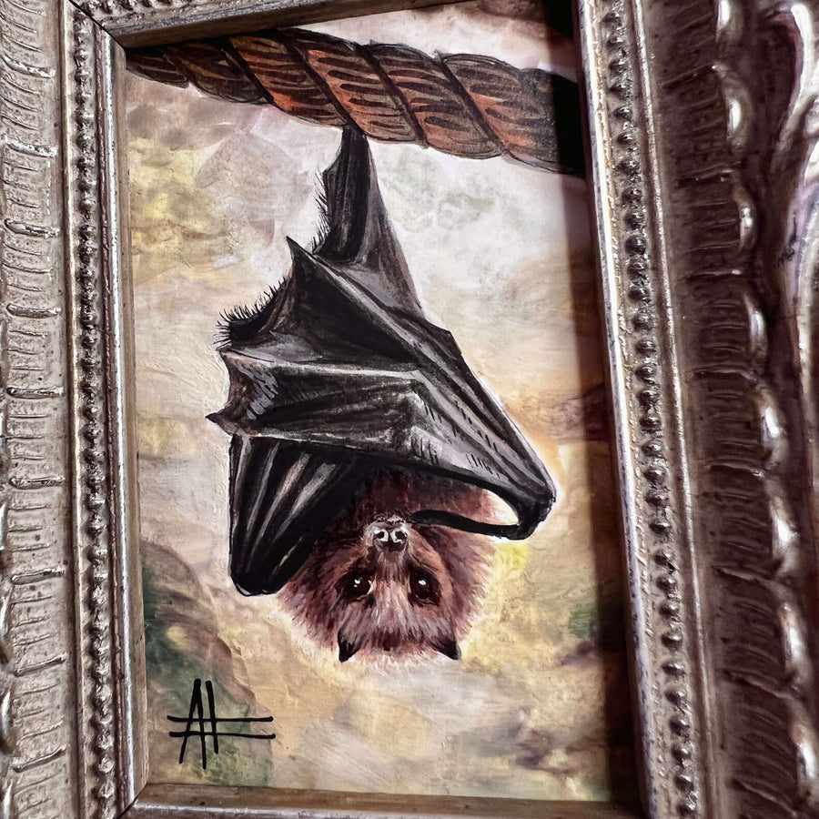 Detailed view of a hanging bat painting with soft textural background in a decorative frame.