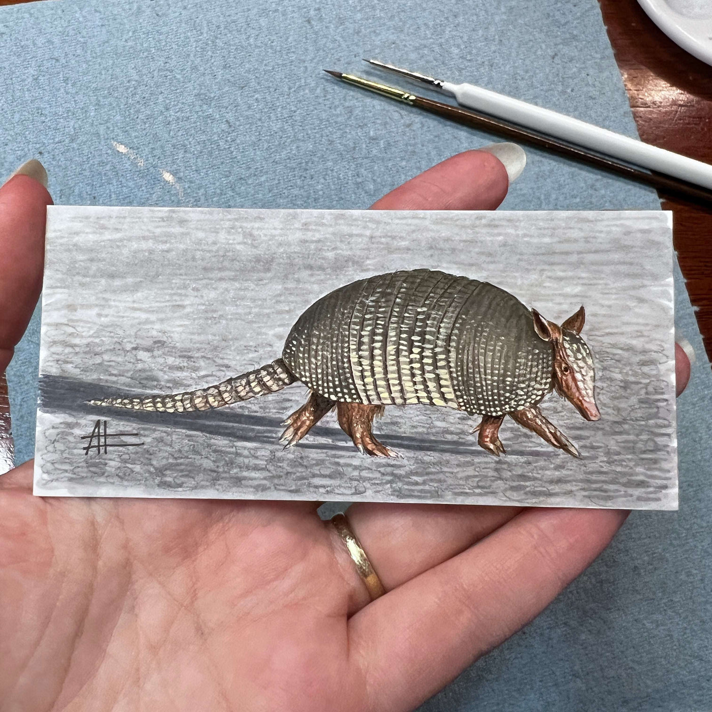 Miniature armadillo painting held in hand, showcasing detailed scale texture.