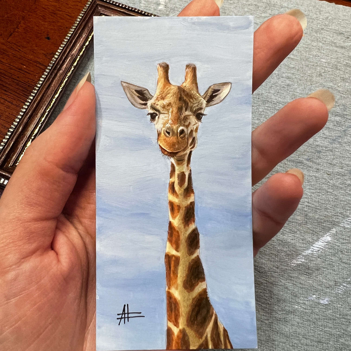 Hand holding a small giraffe painting, showcasing the giraffe's long neck and kind expression.