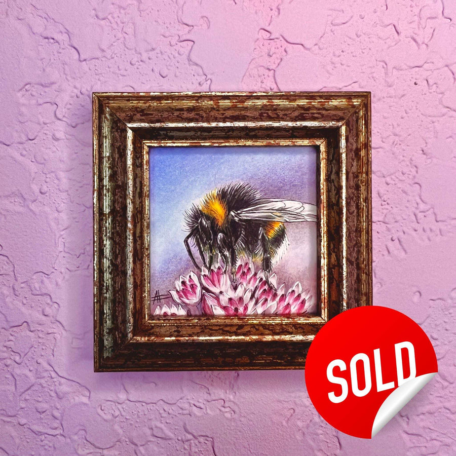 Miniature painting of a bumblebee on a pink flower, framed and displayed on a textured purple wall.