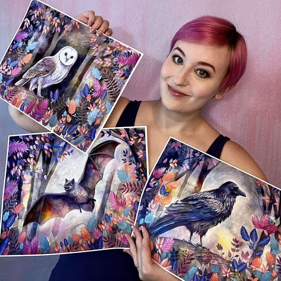 Woman with pink hair holding three large art prints of nocturnal animals surrounded by vibrant foliage.