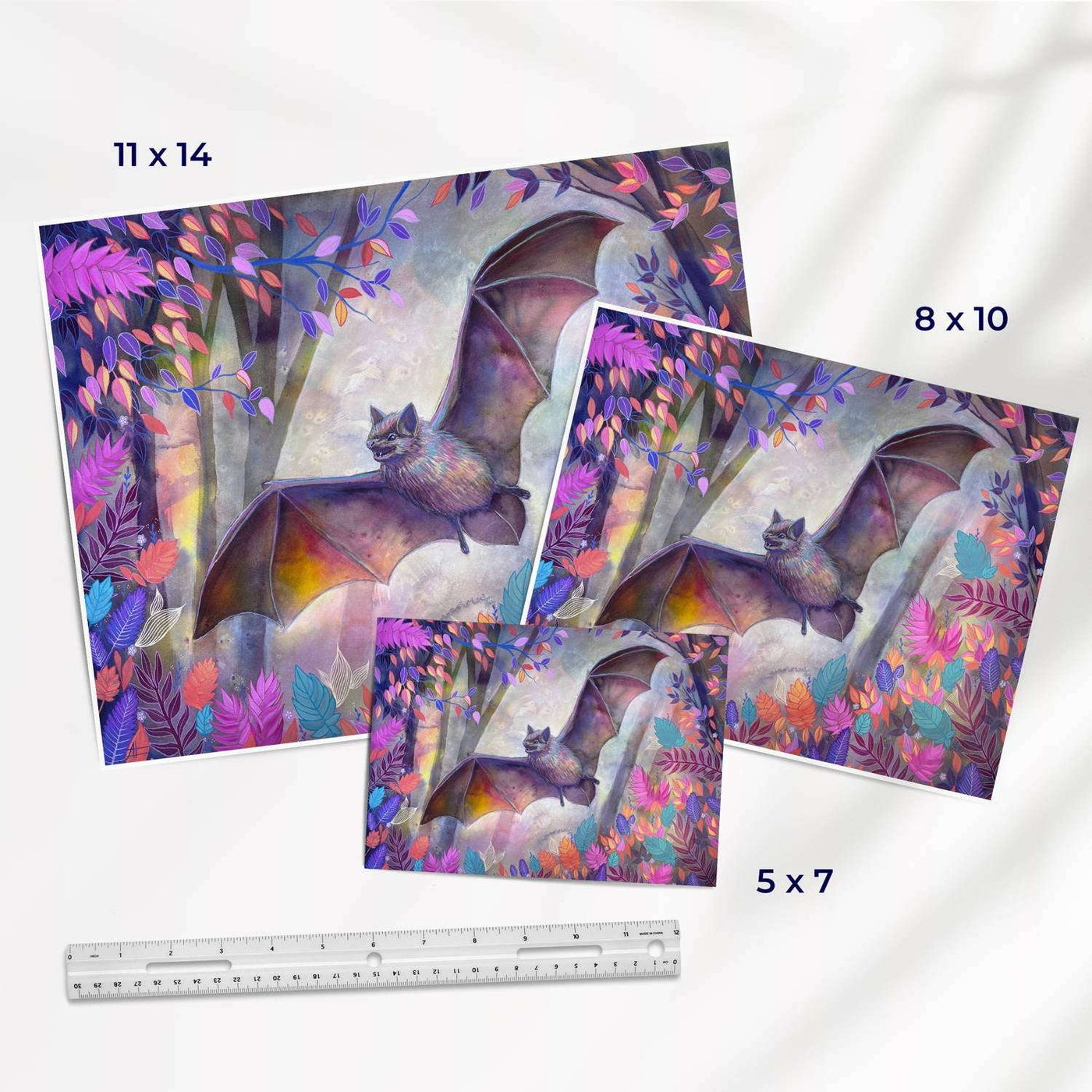 Art prints of various sizes showcasing a bat in a colorful forest, with a ruler for scale.