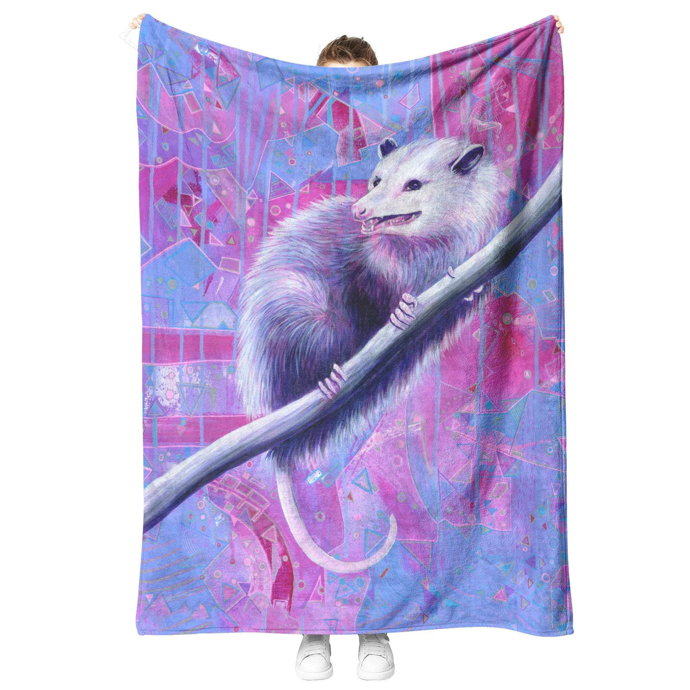 A person stands holding up a large Opossum Blanket featuring a detailed illustration of a white possum on a branch, set against a vibrant, geometric, purple and blue background.