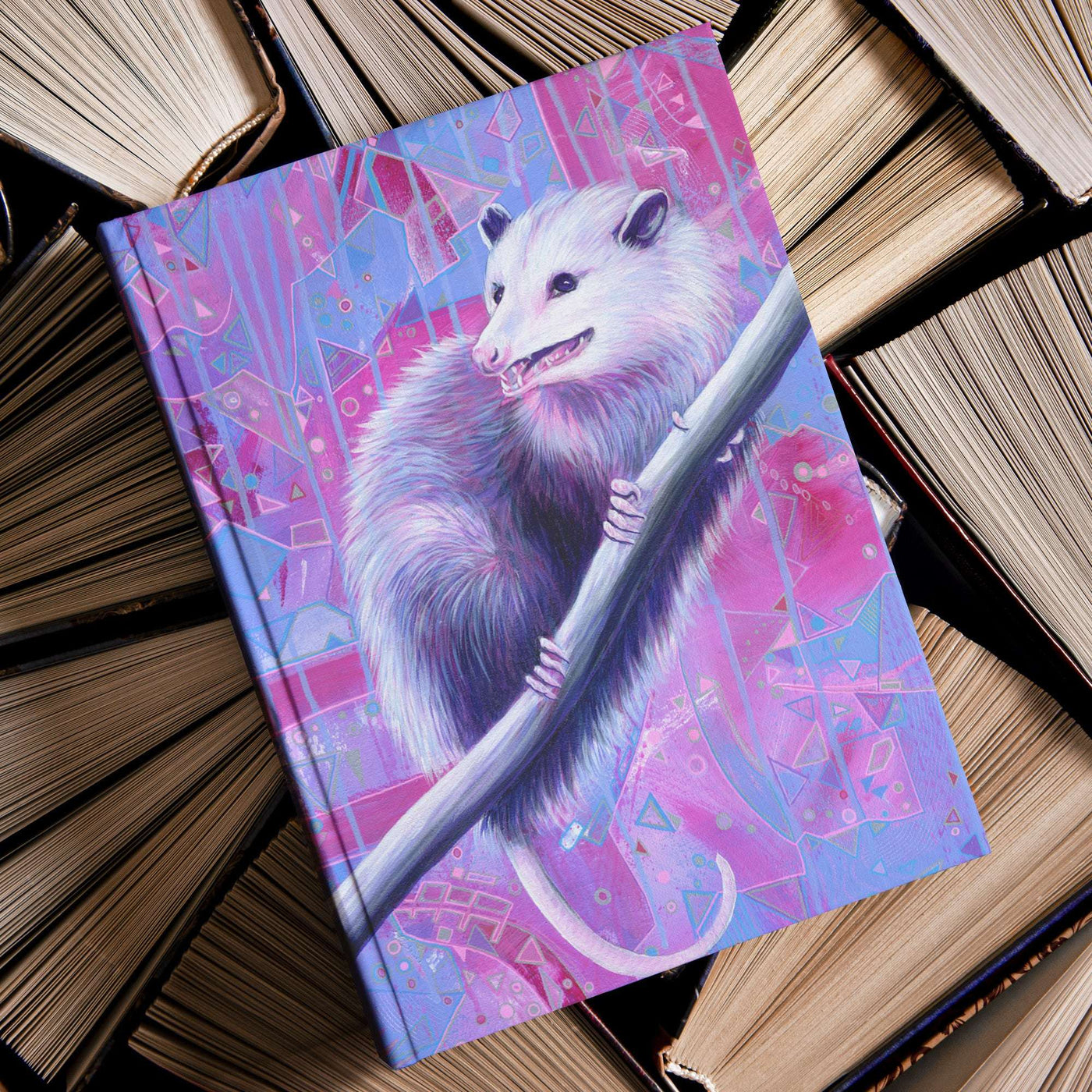 A Opossum Journal with a vibrant illustration of an opossum resting on a tree branch, set on top of a pile of old books.