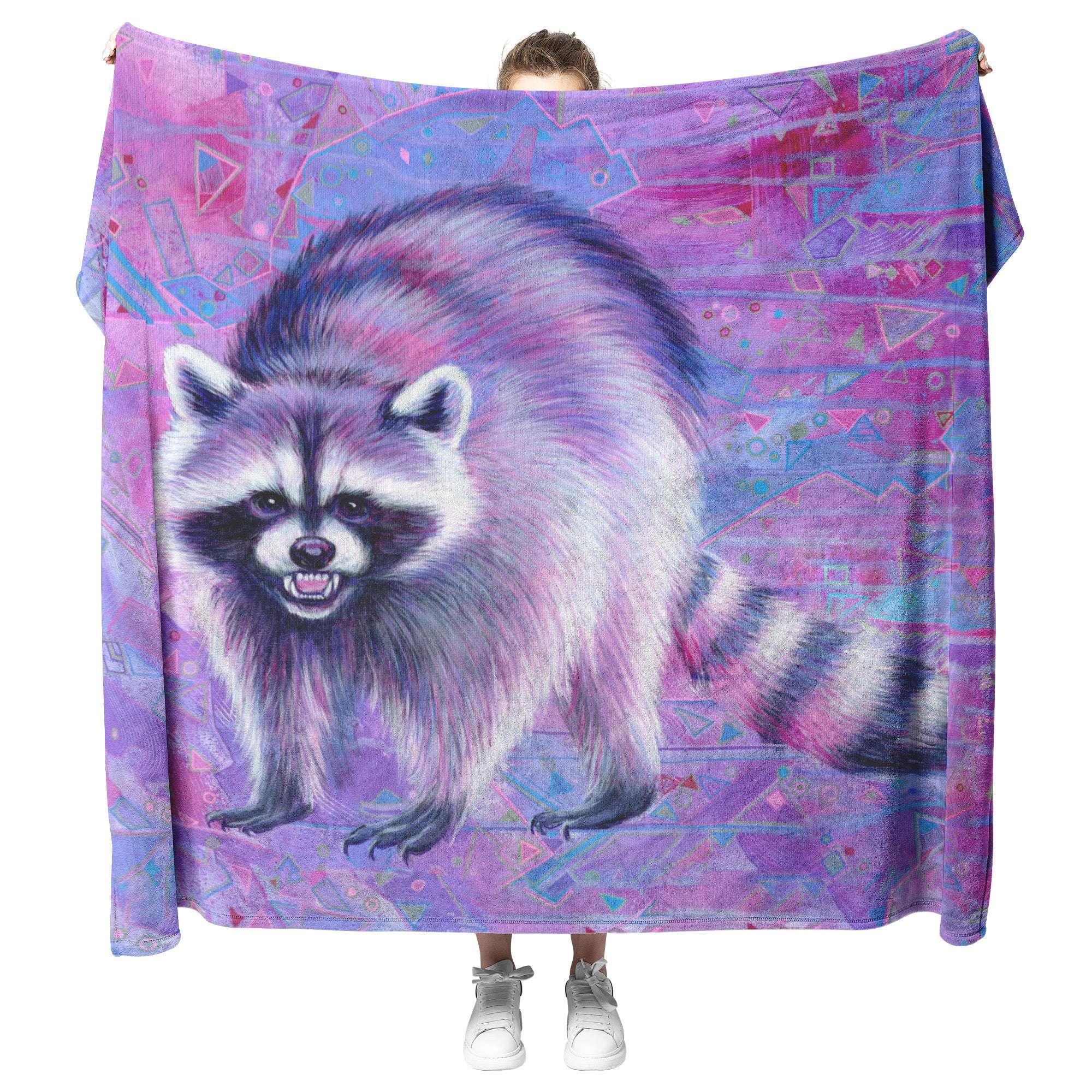 A person holding up a Raccoon Blanket featuring a detailed illustration of a raccoon against a geometric, purple-toned background.