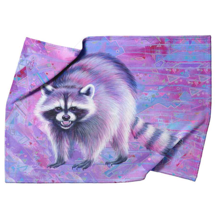 A vibrant Raccoon Blanket with a pink geometric patterned background, displayed on a draped fabric.