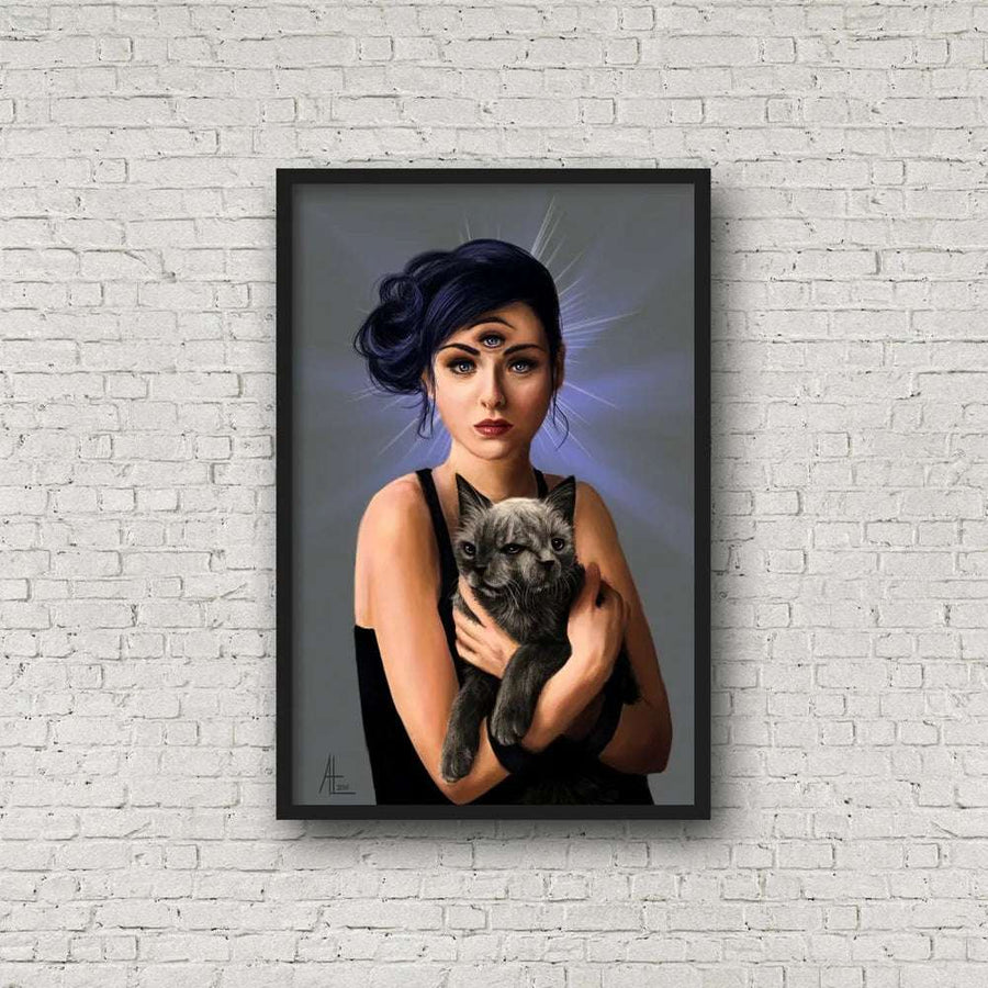 A Third Eye - Art Print, 11x17 of a woman with blue hair holding a small, 2 headed cat, displayed in a black frame on a white brick wall.