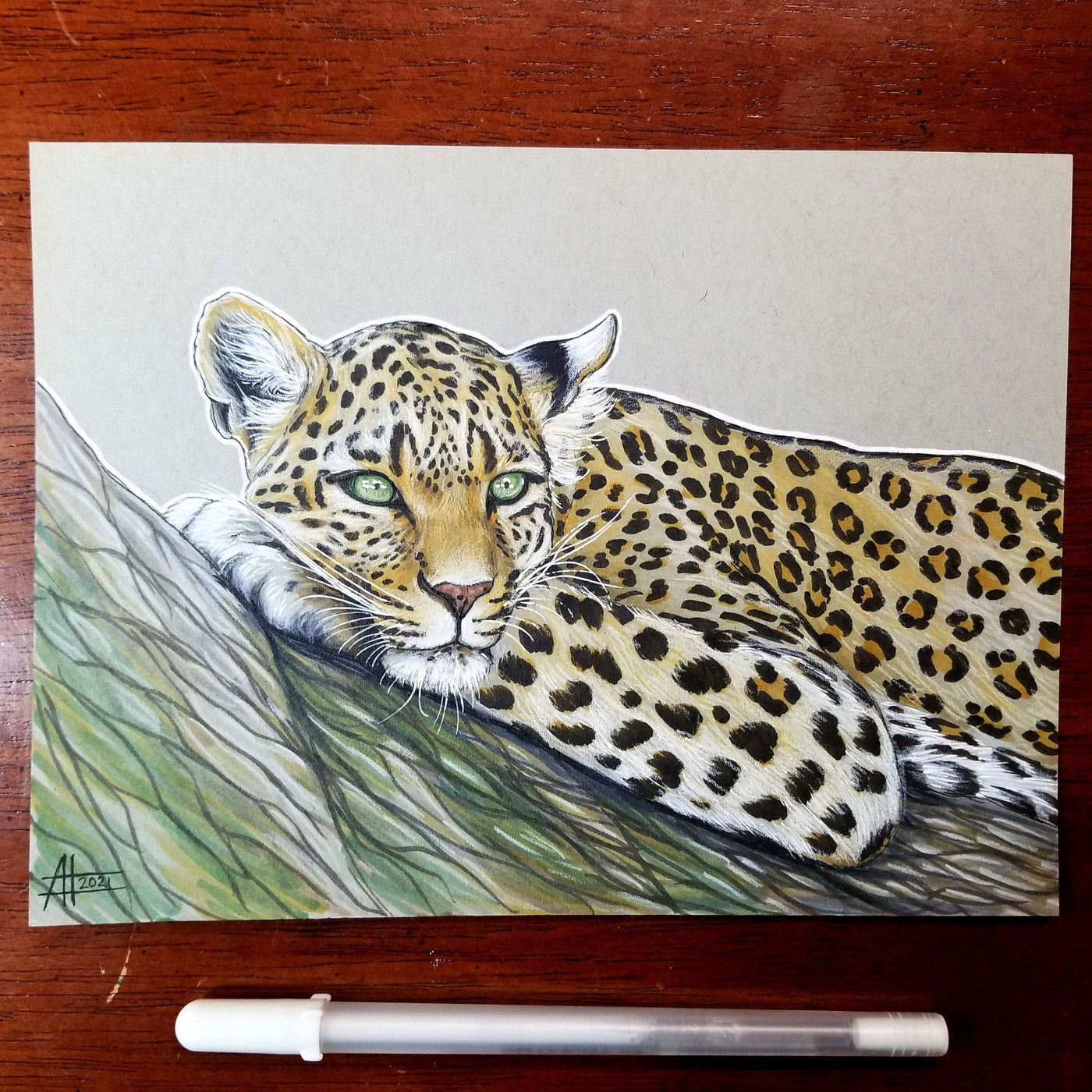 Young Leopard - Original Marker Painting by Amanda Lanford resting on a tree branch, positioned beside a marker pen on a wooden surface.