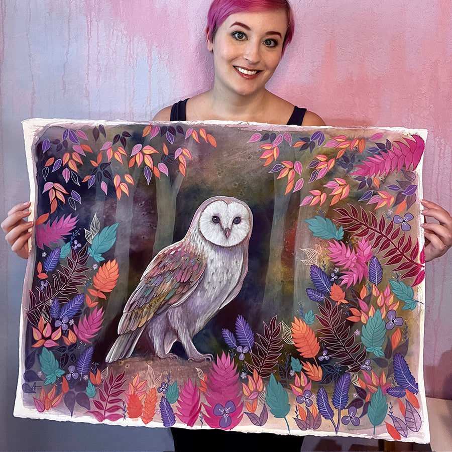 A young woman with short pink hair holding a large, colorful painting of The Owl (Night Flight) surrounded by vibrant foliage.